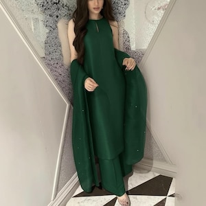 May include: A sleeveless, emerald green outfit consisting of a tunic top, wide-leg pants, and a matching shawl. The top has a keyhole neckline. The shawl is draped over the shoulders. The outfit is made of a smooth, flowing fabric.