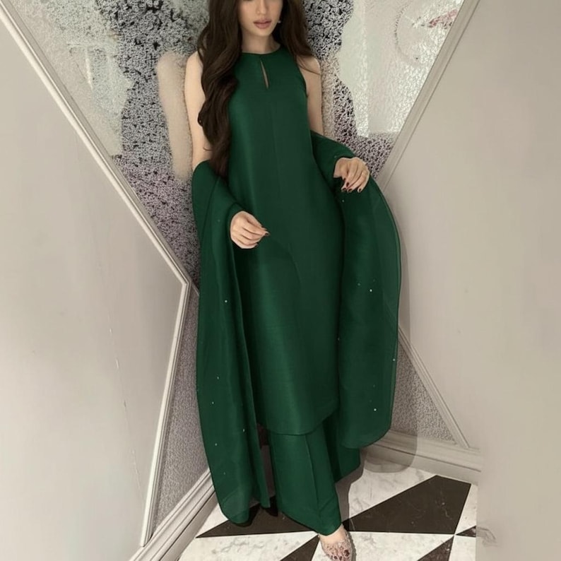 May include: A sleeveless, emerald green outfit consisting of a tunic top, wide-leg pants, and a matching shawl. The top has a keyhole neckline. The shawl is draped over the shoulders. The outfit is made of a smooth, flowing fabric.