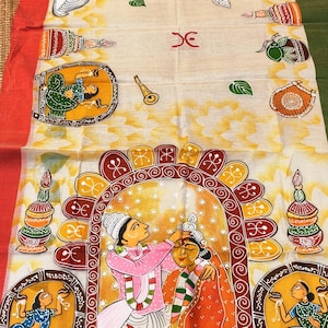 May include: Cream-coloured fabric featuring a detailed, hand-painted design. The artwork shows a wedding scene with figures in traditional dress, framed by decorative patterns and borders in red, green, and yellow. The textile is likely a saree or similar.