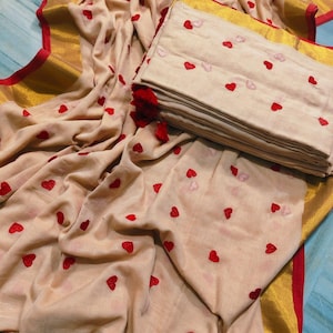 May include: A beige fabric set with red heart embroidery. The set includes a folded stack of fabric and a draped piece, both adorned with the heart pattern. Gold and red trim edges the fabric.