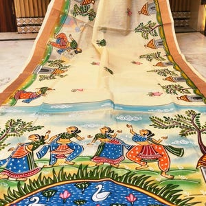 May include: Cream-coloured fabric with a hand-painted design. The artwork shows figures dancing near a pond with swans and lotus flowers. The border has a brown trim with green and blue accents. The overall theme is traditional and artistic.
