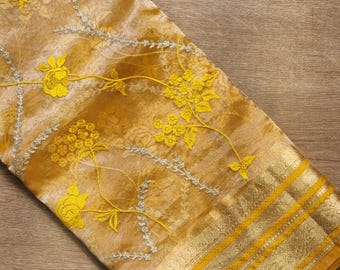 May include: A yellow and gold saree with floral embroidery. The saree has a thin gold border with a repeating pattern.