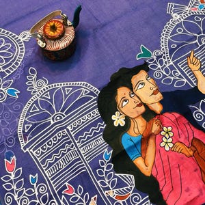 May include: An indigo textile with a hand-painted design featuring a couple and decorative borders. A small, ornate teapot is placed on the fabric. The text "SB2019" is visible.