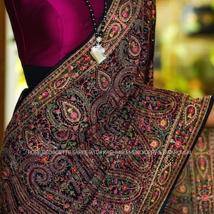Könnte beinhalten: Ein schwarzer Georgette-Sari mit aufwendigen kaschmirischen Stickereien und funkelnden Verzierungen. Der Sari zeigt ein Paisley-Muster in den Farben Rosa, Gold und Blau.