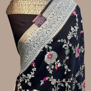 Puede incluir: Un dupatta negro de gasa con un patrón floral en plata, rosa y verde. El dupatta tiene un borde plateado y dorado con un diseño floral.