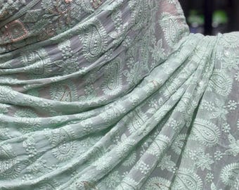 以下が含まれることがあります： 全体に複雑な白い花柄とペイズリー柄の刺繍が施された、ライトミントグリーンのサリー。縁取りにはスカラップエッジとメタリックシルバーのアクセントがあり、レースのトリムが付いた黒いブラウスと組み合わされています。
