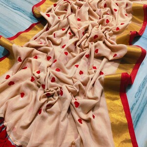 May include: A beige fabric with red heart patterns and a gold border with red trim. The fabric is draped, showing the texture and design. Red tassels are visible at the bottom edge.