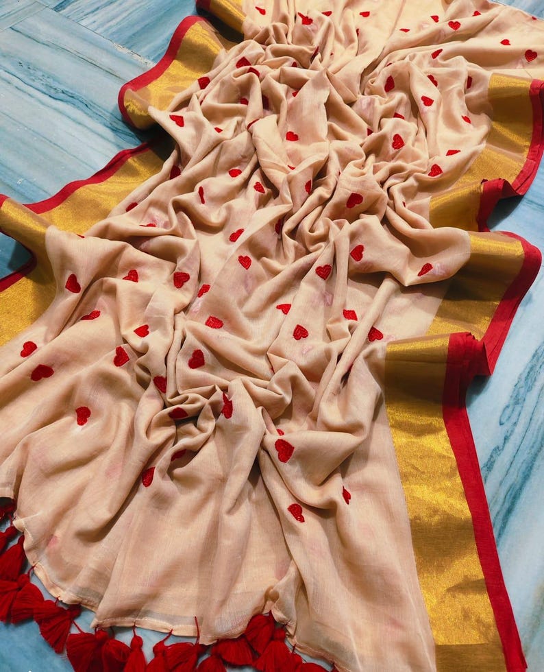 May include: A beige fabric with red heart patterns and a gold border with red trim. The fabric is draped, showing the texture and design. Red tassels are visible at the bottom edge.