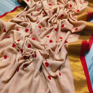 May include: A beige fabric with red heart embroidery. The fabric has a gold border with a red trim. The fabric is draped, showing the texture and design. The overall theme is romantic and feminine.