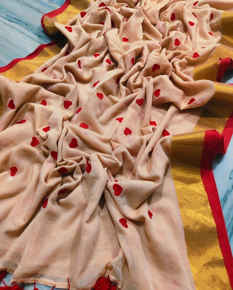 May include: A beige fabric with red heart embroidery. The fabric has a gold border with a red trim. The fabric is draped, showing the texture and design. The overall theme is romantic and feminine.