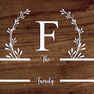 May include: White wooden sign with a floral wreath and the letter F in the center. The text "The Family" is below the letter.