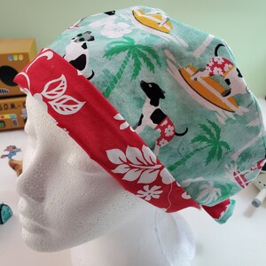 May include: A surgical scrub cap featuring a tropical design. The cap has a light teal background with palm trees and dogs surfing. A red band with white floral patterns accents the cap.