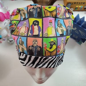 May include: A colorful scrub cap featuring a grid of professional wrestlers in action poses. The cap has a black and white zebra print band. The background is a mix of bright colors, including pink, yellow, and blue.