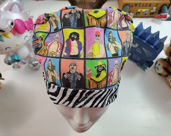 May include: A colorful scrub cap featuring a grid of professional wrestlers in action poses. The cap has a black and white zebra print band. The background is a mix of bright colors, including pink, yellow, and blue.