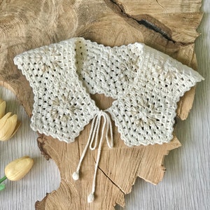 May include: A white crocheted collar with a delicate floral design and gold accents. The collar has a tie closure at the back.