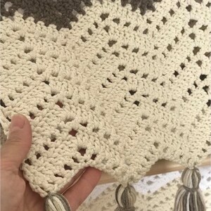 May include: A crocheted throw blanket with a beige and brown color scheme. The blanket has a fringe border and a diamond pattern.