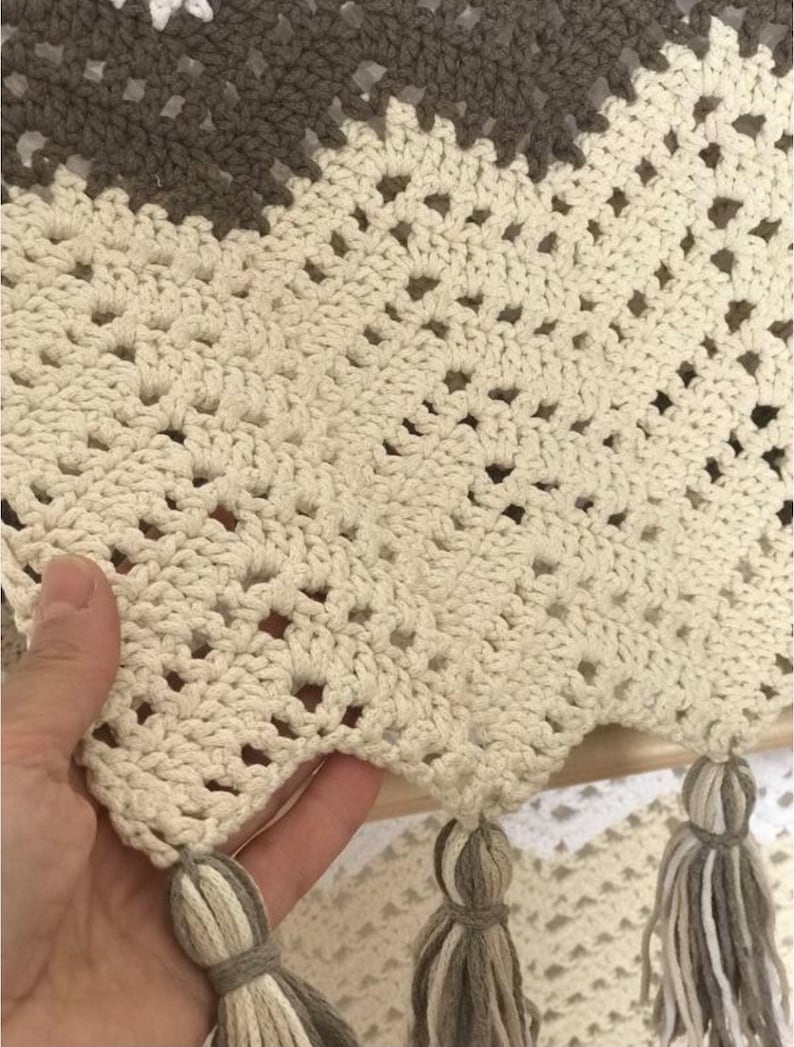May include: A crocheted throw blanket with a beige and brown color scheme. The blanket has a fringe border and a diamond pattern.