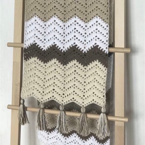 May include: A crocheted throw blanket with a chevron pattern in brown, beige, and white. The blanket has a fringe border with tassels.