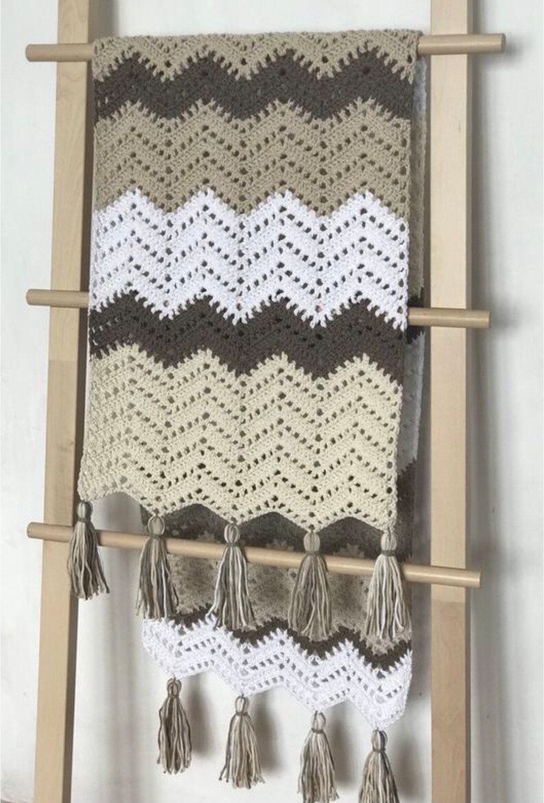 May include: A crocheted throw blanket with a chevron pattern in brown, beige, and white. The blanket has a fringe border with tassels.