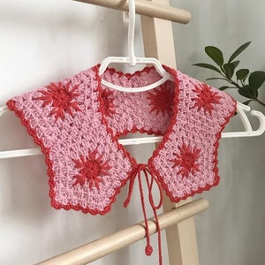 May include: A pink and red crocheted collar with a starburst pattern and a tie closure.