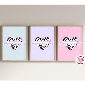 May include: Three framed art prints with a light blue, lavender, and pink background. Each print features a heart with a black and white cow print design and the text "Hyperfocusing". The prints are in wooden frames.