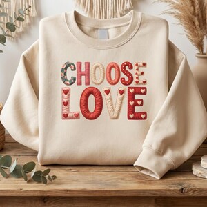 May include: A cream-coloured sweatshirt featuring the phrase "CHOOSE LOVE" in a patchwork design. The letters are in various colours and patterns, including floral, red hearts, and stitched details. A comfortable and fashionable top.