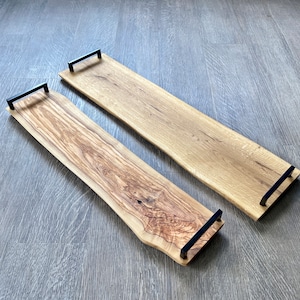 Può includere: Due vassoi da portata in legno con manici in metallo nero. I vassoi sono realizzati in diversi tipi di legno, uno con venature chiare e l'altro con venature scure.