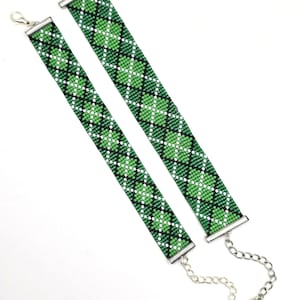 May include: Two beaded bracelets with a green, black, and white diamond pattern. The bracelets have silver-colored clasps and chain extenders. The design features a repeating four-leaf clover motif.