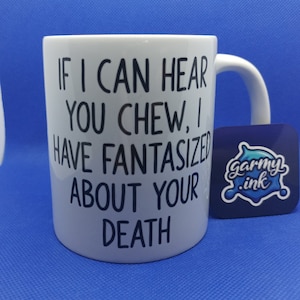 以下が含まれることがあります： 白いセラミック製のマグカップに、黒い文字で「もし君が噛む音が聞こえたら、僕は君の死を夢見てきたんだ」と書かれている。マグカップには、白い文字で「garmy.ink」と書かれた青いステッカーが貼られている。