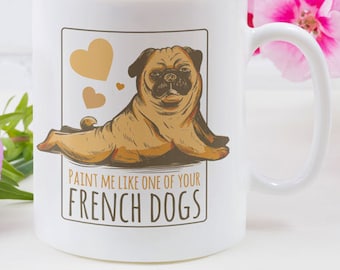 Könnte beinhalten: Weiße Keramiktasse mit einer Illustration einer französischen Bulldogge und dem Text "Paint me like one of your French Dogs". Die Tasse steht vor rosa Blumen.