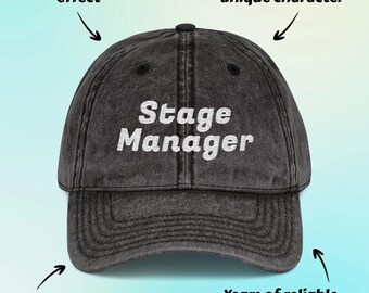 May include: A washed black baseball cap with the text "Stage Manager" in white. The cap is made of 100% cotton twill and has a vintage effect. It is designed for years of reliable wear.