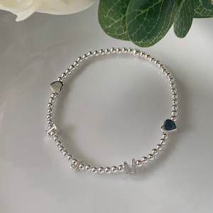 May include: A silver beaded bracelet with the letters "MOM" and two heart charms.