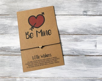 以下が含まれることがあります： 赤いハートと「Be Mine」の文字が書かれた茶色のカード。カードには、小さな白いハートのチャームが付いた黒い紐が結ばれています。カードには、紐を使って願い事を叶えるための説明が書かれています。カードの文章は、「Little Wishers 目を閉じて願い事をし、それからこれを足首か手首に結びます。紐が二つに切れたら、願い事が叶うと言われています！」です。