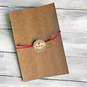 May include: A brown paper envelope tied with red string and a round, brown paper sticker with a red heart and the text "Hand Made With Love, thank you, Especially For You".