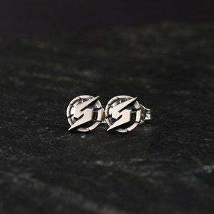 Puede incluir: Un par de pendientes de botón de plata con un diseño de rayo estilizado.