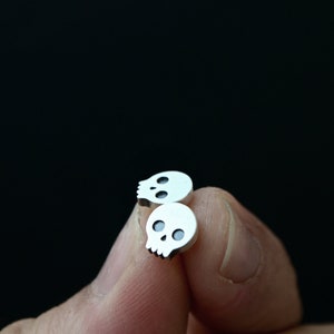 May include: A pair of silver skull stud earrings. The earrings are small and have a simple design.