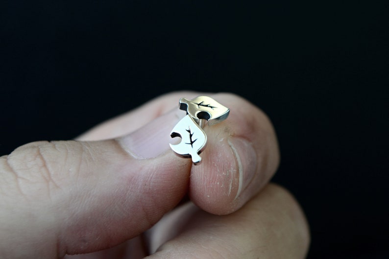 May include: A pair of silver leaf-shaped earrings with a small branch design.