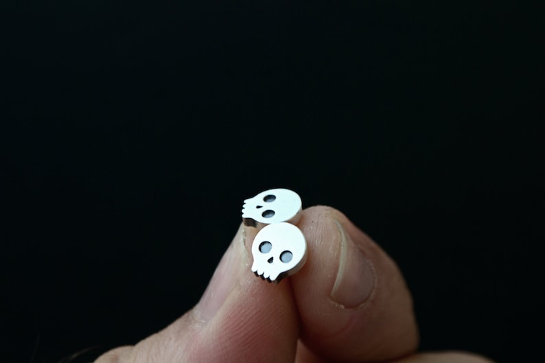 May include: A pair of silver skull stud earrings. The earrings are small and have a simple design.
