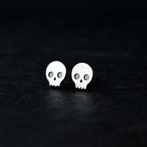 May include: A pair of silver skull stud earrings. The earrings are small and have a simple design.