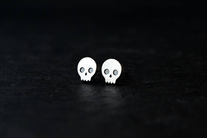May include: A pair of silver skull stud earrings. The earrings are small and have a simple design.