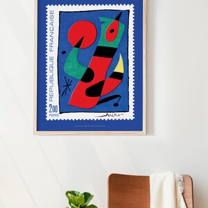 May include: A framed poster of a colorful abstract painting by Joan Mir&oacute;. The painting features a red, green, yellow, and black abstract figure on a blue background. The poster is titled "Republique Fran&ccedil;aise" and features the text "2.00 Postes".