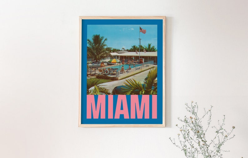 May include: Framed vintage-style poster featuring a pool scene in Miami. The image has a blue border and the word "MIAMI" in pink block letters at the bottom. The scene includes palm trees, a pool, and an American flag.