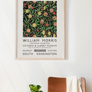 May include: A vintage poster advertising a William Morris Centenary Exhibition at the Victoria & Albert Museum in London. The poster features a black and white illustration of a citrus fruit pattern with green leaves and red flowers. The text on the poster reads "William Morris Centenary Exhibition Victoria & Albert Museum Feb. 10th to April 8th Admission Free Nearest Underground Station South Kensington."