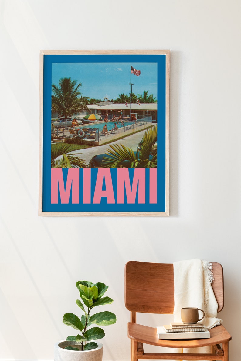 May include: A framed print featuring a vintage-style image of a pool scene in Miami. The image has a blue border and the word "MIAMI" in pink block letters. The scene includes palm trees, a pool, and people.