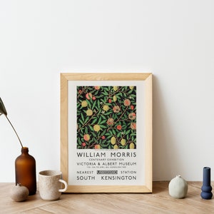 May include: A framed print of a vintage poster for a William Morris exhibit at the Victoria & Albert Museum. The poster features a floral design with pomegranates and lemons on a dark green background. The text on the poster reads "William Morris, Centenary Exhibition, Victoria & Albert Museum, Nearest South Kensington Station".