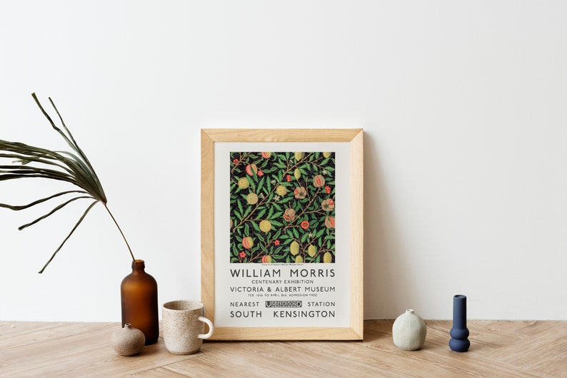 May include: A framed print of a vintage poster for a William Morris exhibit at the Victoria & Albert Museum. The poster features a floral design with pomegranates and lemons on a dark green background. The text on the poster reads "William Morris, Centenary Exhibition, Victoria & Albert Museum, Nearest South Kensington Station".