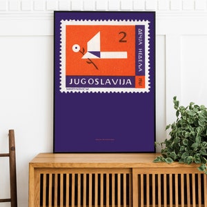 May include: A vintage poster featuring a purple stamp with a red and white dove design. The stamp reads "JUGOSLAVIJA" and "2 DINARA" in white text. The poster is framed in black and displayed on a wooden shelf.