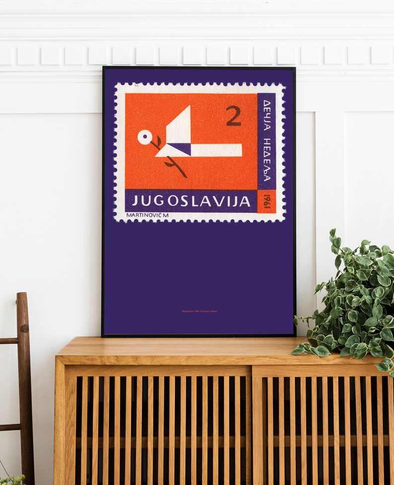 May include: A vintage poster featuring a purple stamp with a red and white dove design. The stamp reads "JUGOSLAVIJA" and "2 DINARA" in white text. The poster is framed in black and displayed on a wooden shelf.