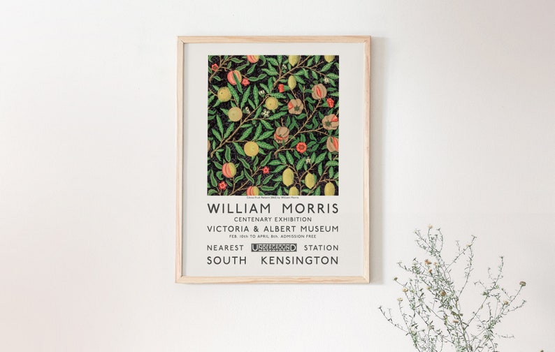 May include: A framed poster advertising a William Morris Centenary Exhibition at the Victoria & Albert Museum. The poster features a colorful floral pattern with green leaves, yellow lemons, and red flowers on a black background. The text on the poster reads "William Morris Centenary Exhibition Victoria & Albert Museum Feb 1st to April 1st, Admission Free Nearest Underground Station South Kensington."