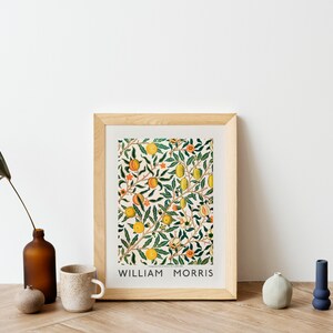 Puede incluir: Una impresi&oacute;n enmarcada de un patr&oacute;n floral con frutas y hojas de color naranja, amarillo y verde. La impresi&oacute;n est&aacute; titulada "William Morris".